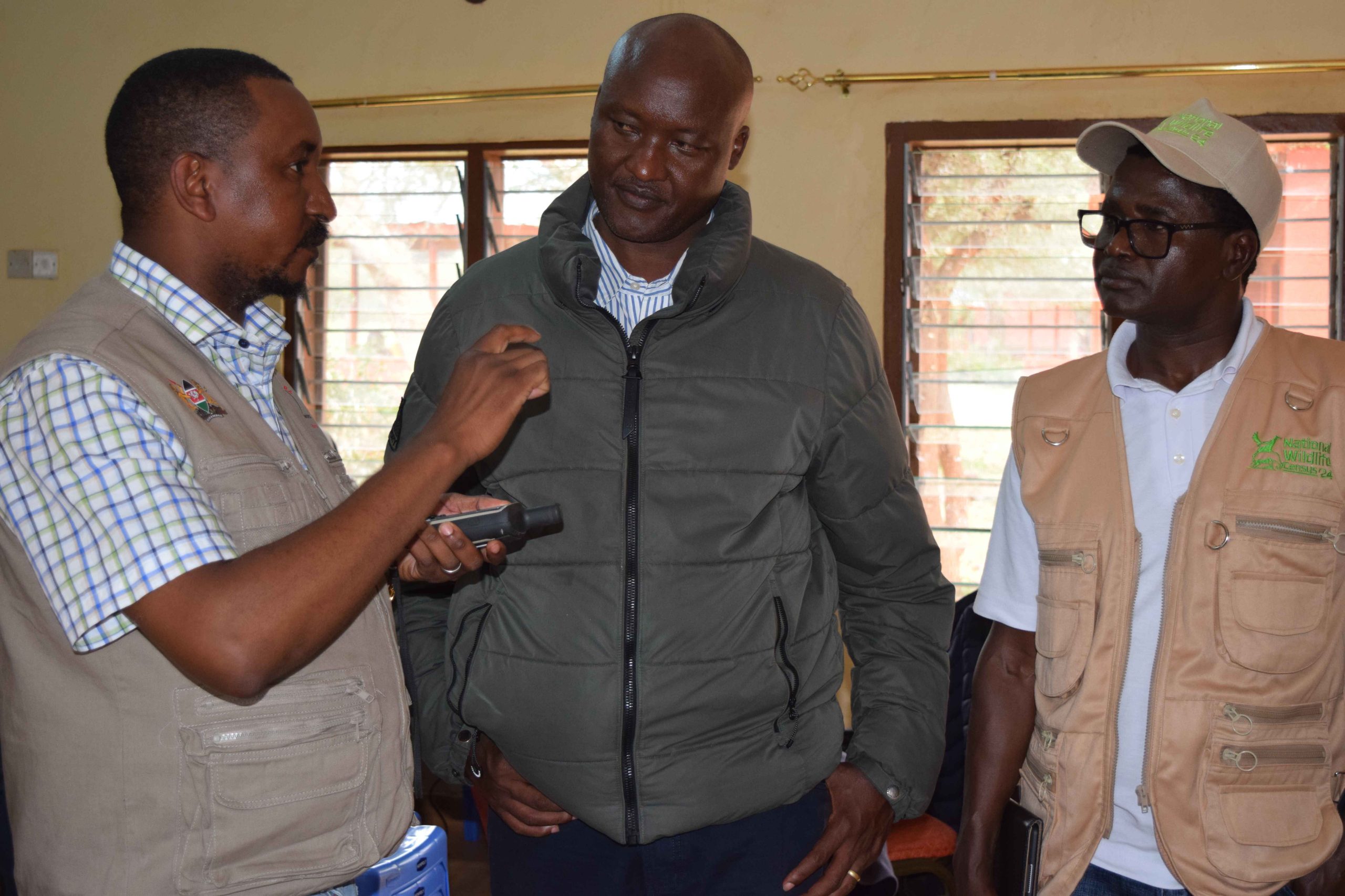 Secretary Conservation for the State Department for Wildlife Dr John Chumo (middle) given a brief by Wildlife scientist Stephen Ndamuki (left) of how Global Positioning (GPS) is applied in wildlife census as Wildlife Research and Training Institute Deputy Director, Dr David Ndeere (right) looks on.